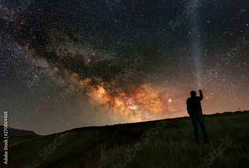 Beautiful starry night, man silhouette stands on in the hill and looks at the Milky Way galaxy.