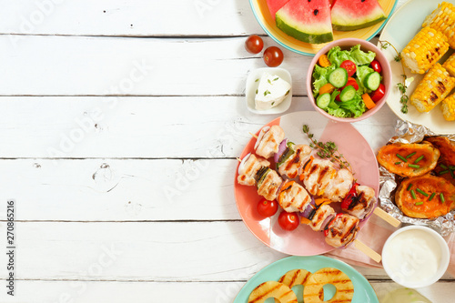 Summer BBQ or picnic food side border. Selection of grilled meat, fruits, salad and potatoes. Top view over a white wood background. Copy space.