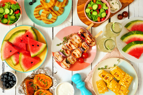 Summer BBQ or picnic food concept. Selection of grilled meat, fruits, salad and potatoes. Top view table scene over a white wood background.