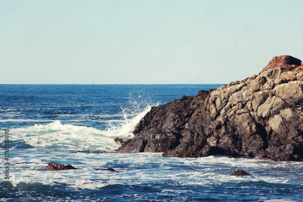 Splash waves sea hitting rocks on the beach with blue sky