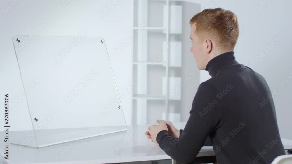 Rare view of young Caucasian man sitting at desk at invisible AR interface and having online conversation. Suitable for adding augmented reality graphics Rare view of young Caucasian man sitting at desk at invisible AR interface and having online conversation. Suitable for adding augmented reality graphics