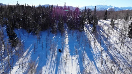 Panoramic aerial shot of Heber Valley mountains trees and snowscooters. This video shows mountains of Heber Valley on the horizon and trees with two snowmachines.