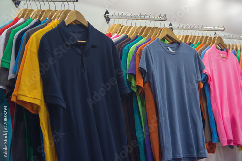 Variety of t-shirts of different colors on wooden hangers