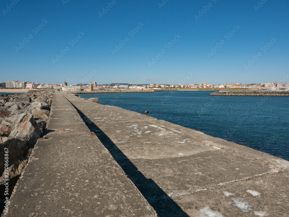 View along harbor wall in Povoa de Varzim, Portugal with sea and harbor on right and city in distance
