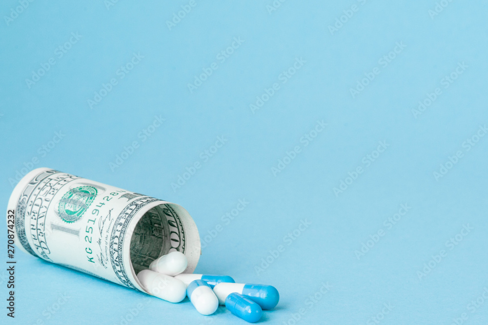 Money dollar rolled up with pills flowing out isolated on blue background, high costs of expensive medication concept. Copy space Money dollar rolled up with pills flowing out isolated on blue background, high costs of expensive medication concept. Copy space