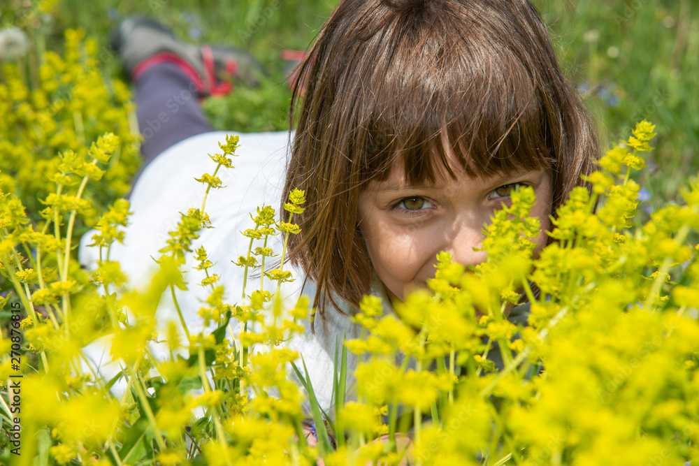 Cute little girl lying in the grass and flowers and laughing Cute little girl lying in the grass and flowers and laughing
