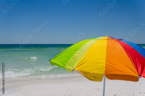 Colorful umbrella at ocean beach shoreline. Scenic tourist travel destination with bright sun protection. Relax and enjoy sun and surf during vacation getaway. © hildeanna