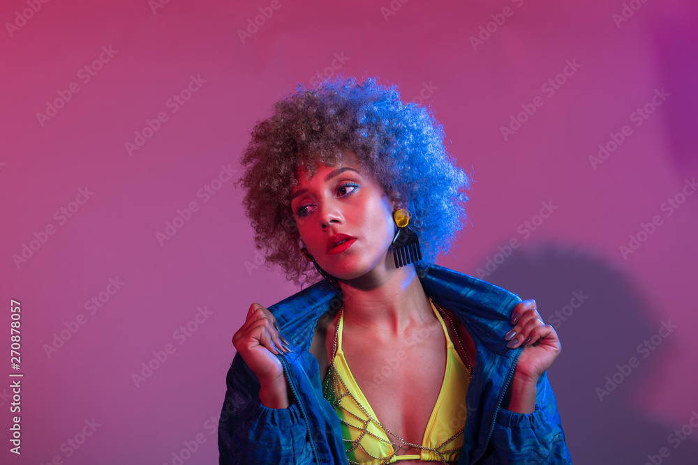 Funky young black woman with neon colored bikini modeling in studio lights setting, with blue windbreaker jac