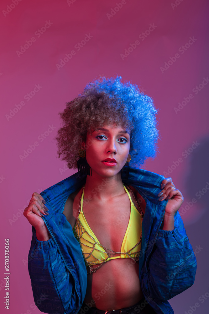 Funky young black woman with neon colored bikini modeling in studio lights setting, with blue windbreaker jac Funky young black woman with neon colored bikini modeling in studio lights setting, with blue windbreaker jac