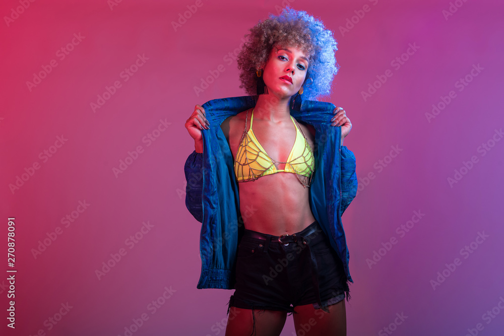Funky young black woman with neon colored bikini modeling in studio lights setting, with blue windbreaker jac Funky young black woman with neon colored bikini modeling in studio lights setting, with blue windbreaker jac
