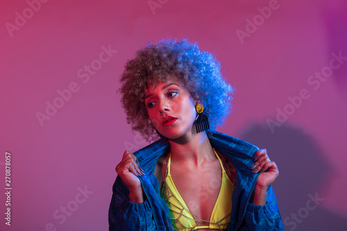 Funky young black woman with neon colored bikini modeling in studio lights setting, with blue windbreaker jac © Adrian Coto