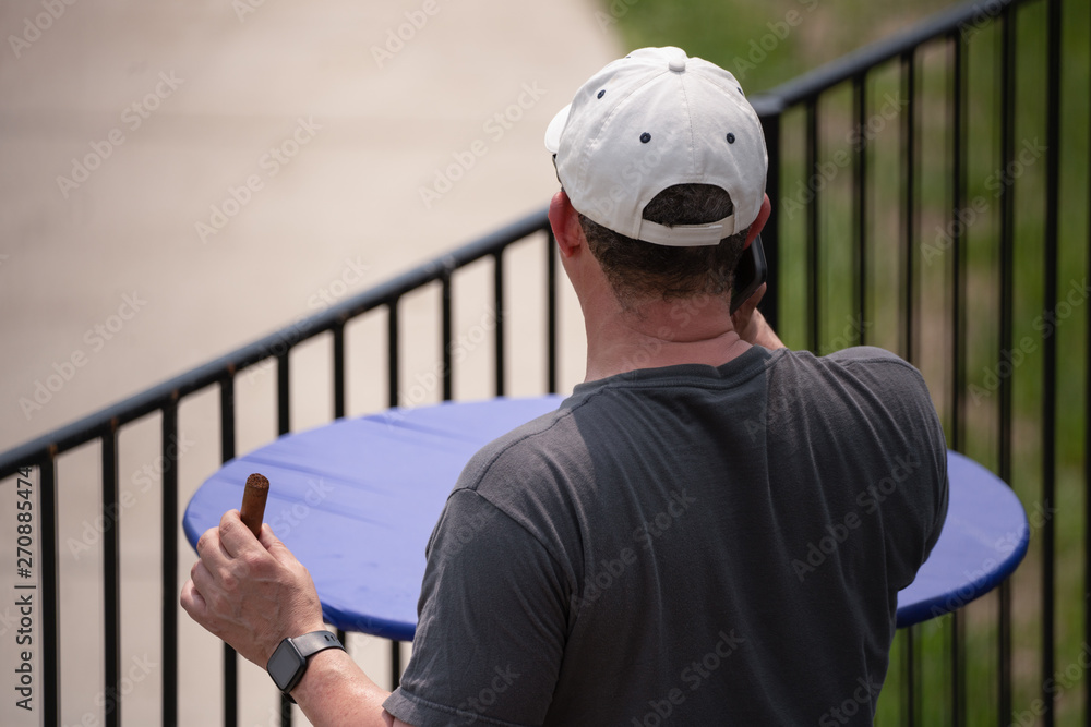 unknown man smokes cigar while talking on cell phone unknown man smokes cigar while talking on cell phone