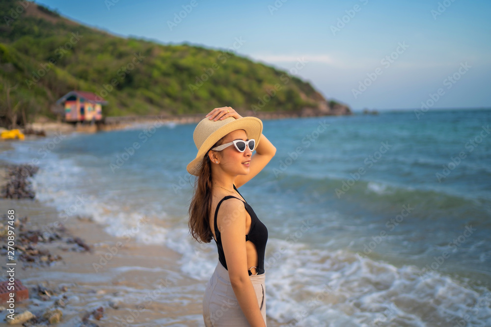 relaxing time concept with traveler girl posing smile in the sea beach in beautiful sunset time by wear sunglass and hat