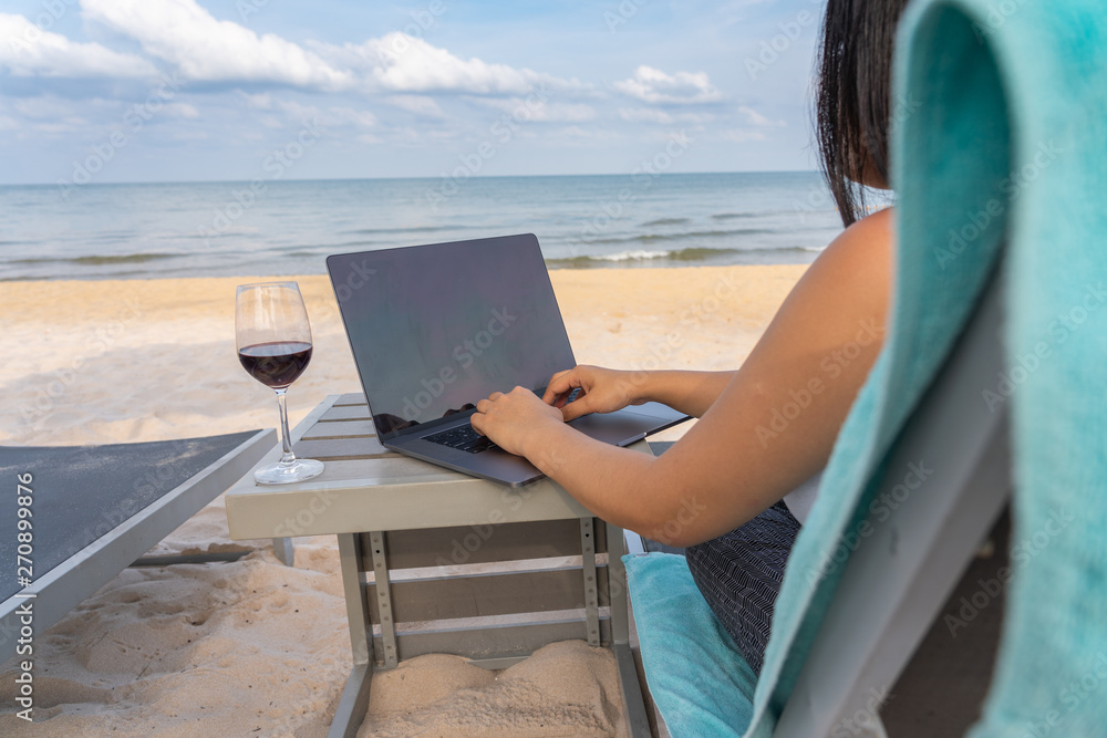 Woman hands typing on laptop with a glass of wine on table