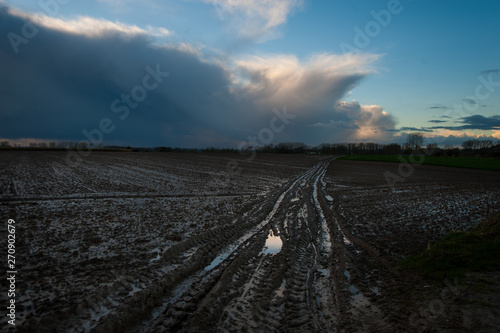 A flooded country road, in the flemish country side, against a clouy sky.