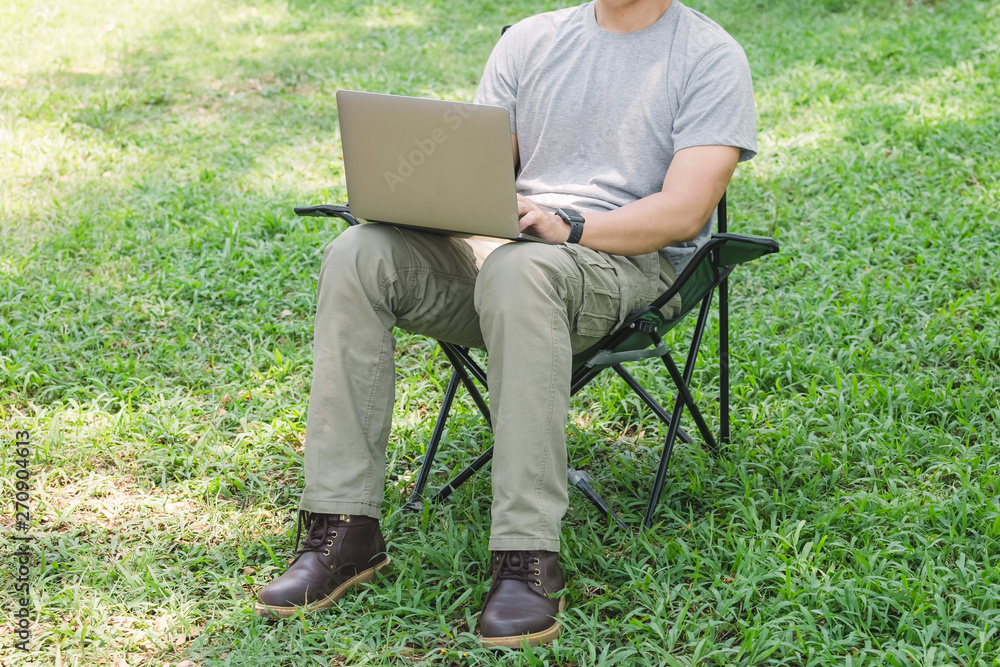 man sitting on camping chair and working with laptop computer in the garden man sitting on camping chair and working with laptop computer in the garden