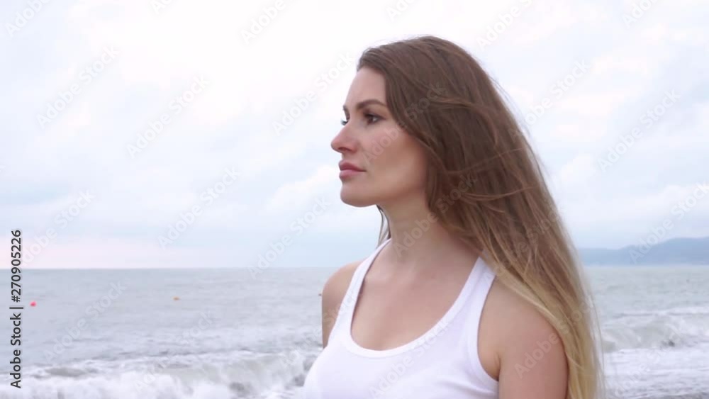 Blonde girl dressed a white top is walking on the beach on cloudy day Blonde girl dressed a white top is walking on the beach on cloudy day