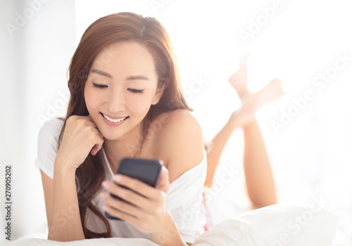 young smiling woman watching mobile phone on bed