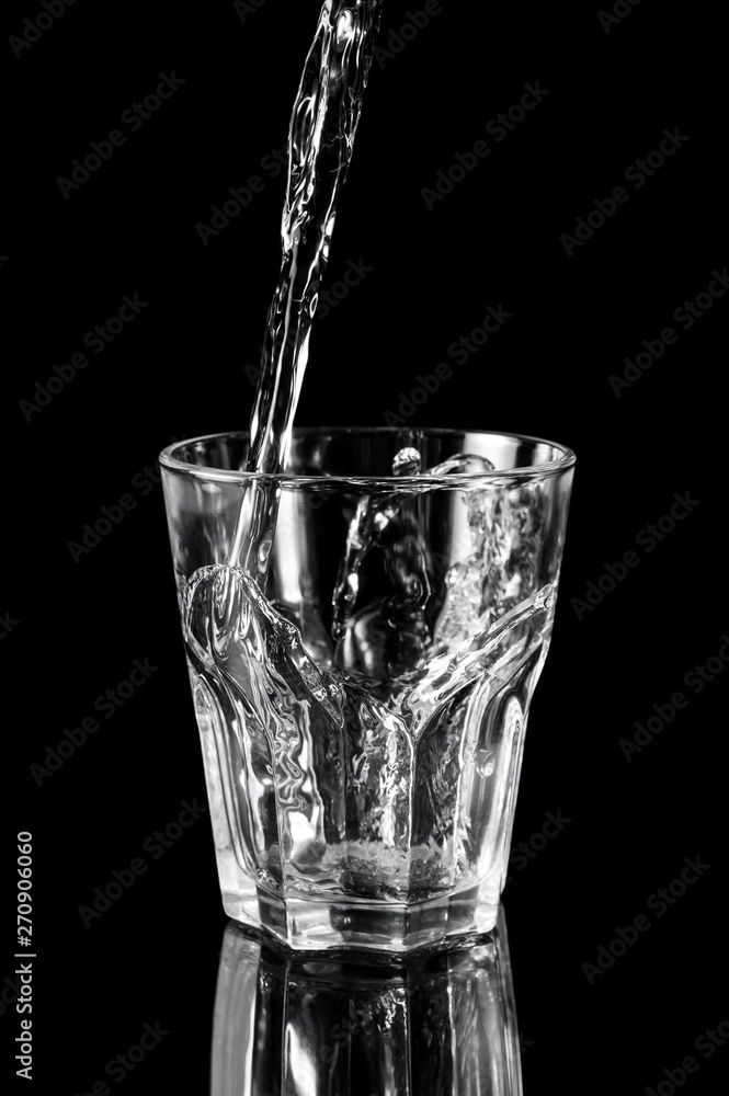Water pouring into the glass on black reflective background. Water pouring into the glass on black reflective background.