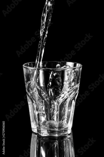 Water pouring into the glass on black reflective background.