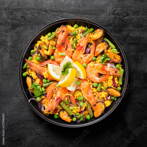 Traditional spanish seafood paella in the fry pan on a black wooden table, top view.