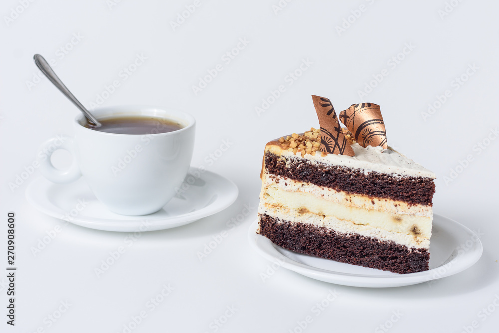 A piece of cake with chocolate and caramel on a plate and a mug of tea on a white background A piece of cake with chocolate and caramel on a plate and a mug of tea on a white background