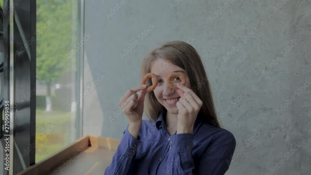 The girl brings onion rings to her face and smiles in a fast-food restaurant. The girl brings onion rings to her face and smiles in a fast-food restaurant.