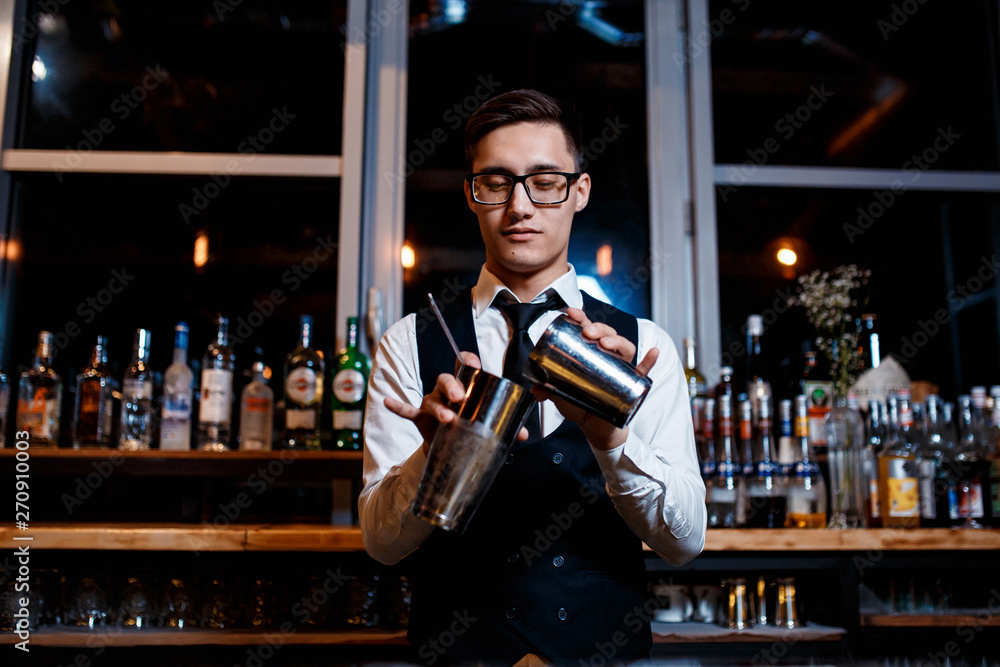elegant young male barman prepares a delicious cocktail at the bar