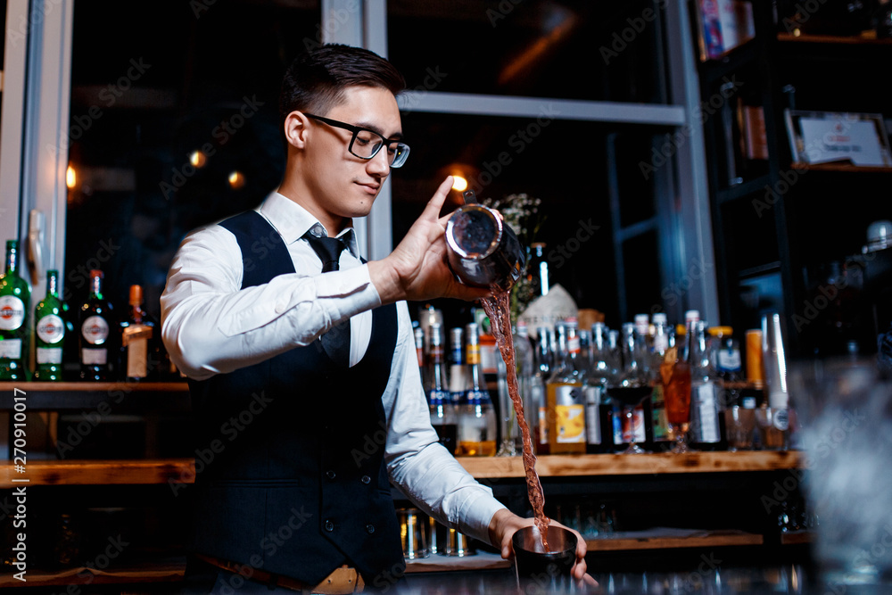 elegant young male bartender preparing a delicious cocktail at the bar. Bartender enjoys high cocktail