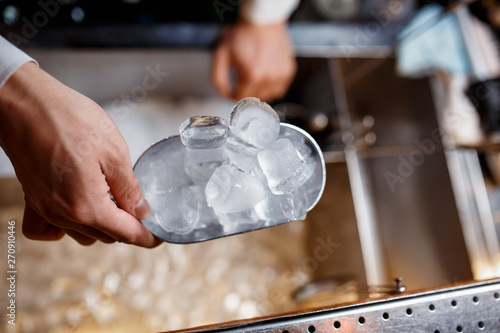 bartender scoops up ice for making alcoholic cocktails. close-up