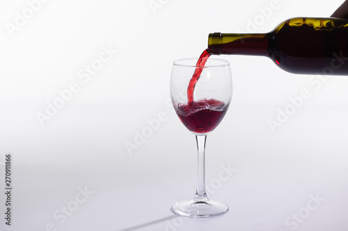 Red wine pouring into glass from bottle on white background with copy space