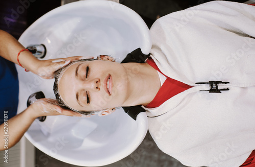 beauty and people concept - happy young woman with hairdresser washing head at hair salon