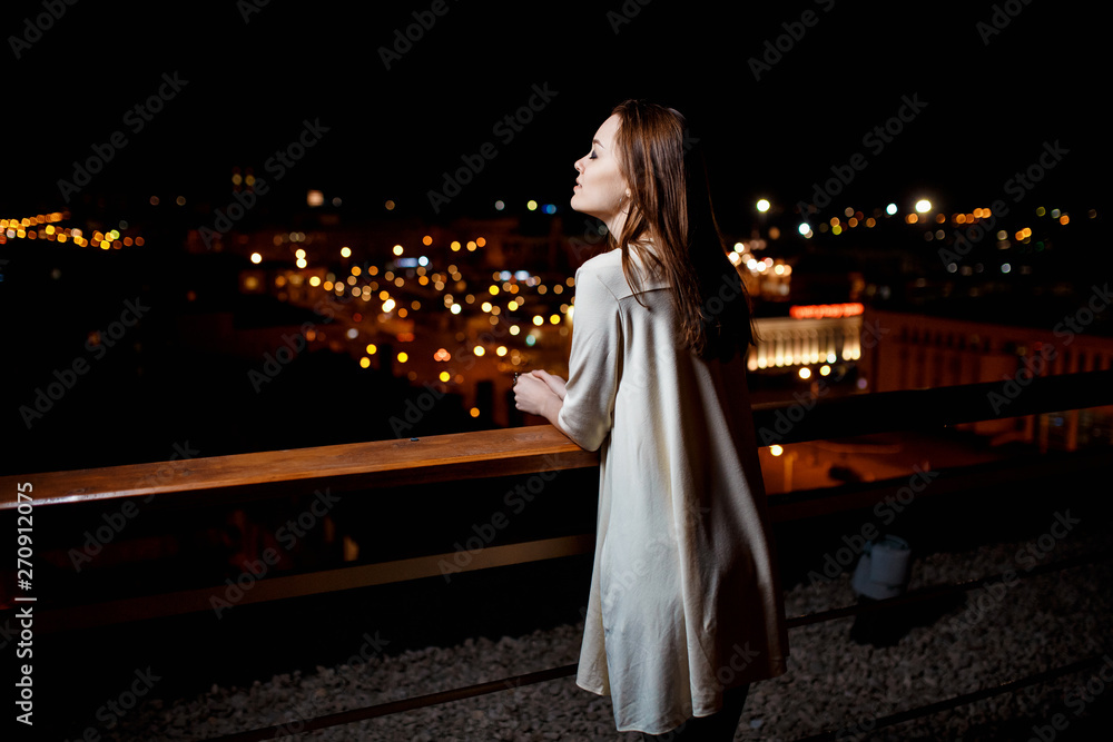 Obraz premium young girl with a cocktail in her hands on the terrace of the bar on the background of the night city.