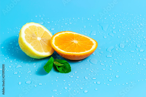 Slices of orange and lemon with mint leaves on a blue background with water drops. Summer cool water orange slices.
