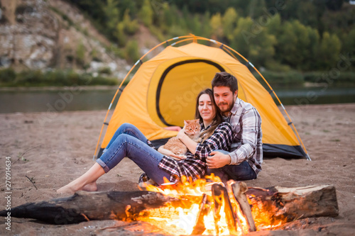 people, summer tourism and nature concept - couple near camp fire warming up seen from the tent © satura_