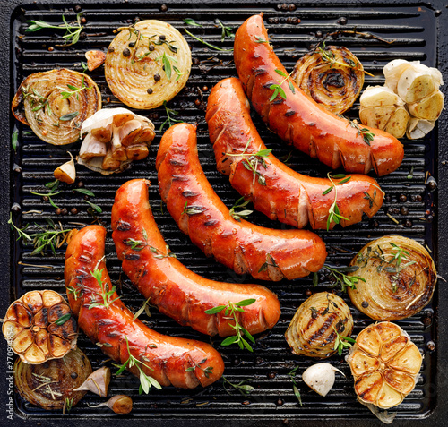 Fotografie, Obraz Grilled sausage with the addition of herbs and vegetables on the grill plate, top view