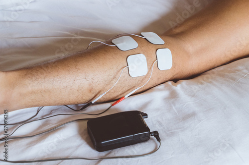 Patient applying electrical stimulation therapy on leg. Electrical tens. photo