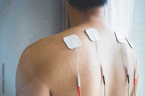 TENS treatment in physical therapy. Young man with TENS on his back and shoulders.