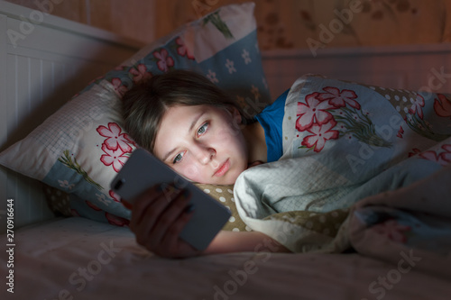 Cropped indoor portrait of young sleepy girl in a bed. Woman can't sleep and using smartphone, suffer from insomnia. Sleepy tired, social media addiction, cell phone dependency, sleeplessness concept.