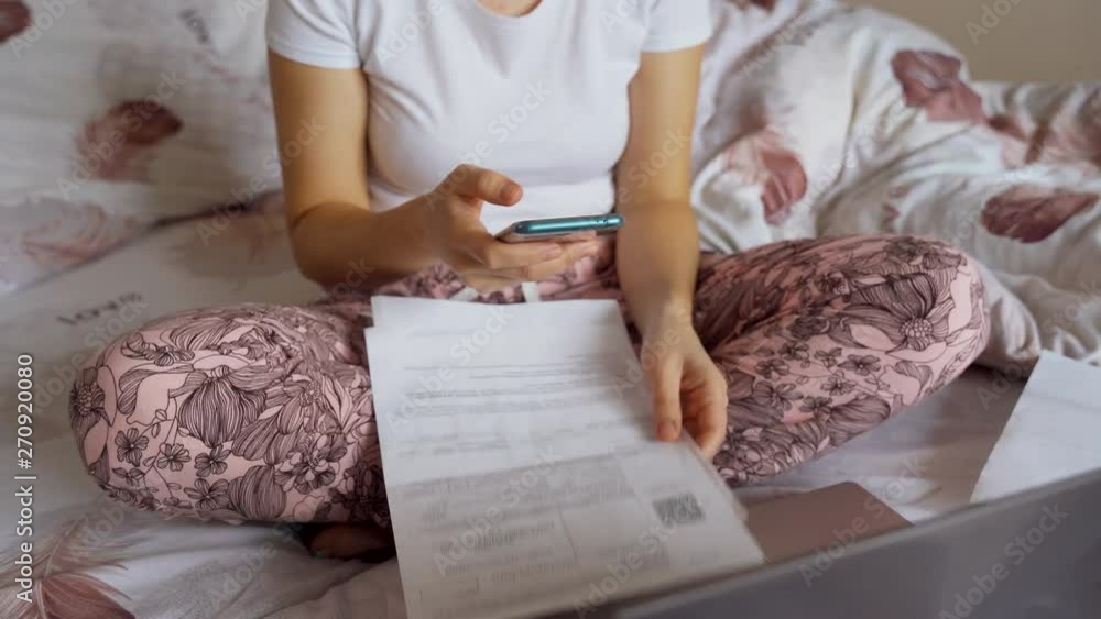 A woman in bed is scanning a barcode using a smartphone to pay for utilities. Woman in pajamas. A woman in bed is scanning a barcode using a smartphone to pay for utilities. Woman in pajamas.