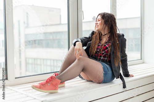 Young stylish woman with dreadlocks sitting on the windowsill