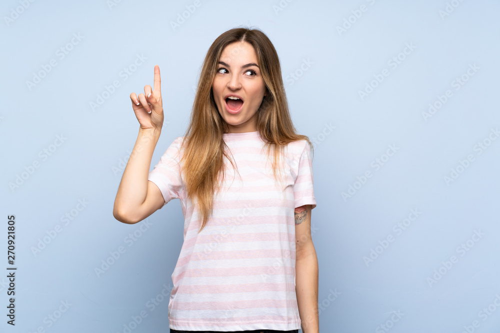 Fototapeta premium Young woman over isolated blue background intending to realizes the solution while lifting a finger up