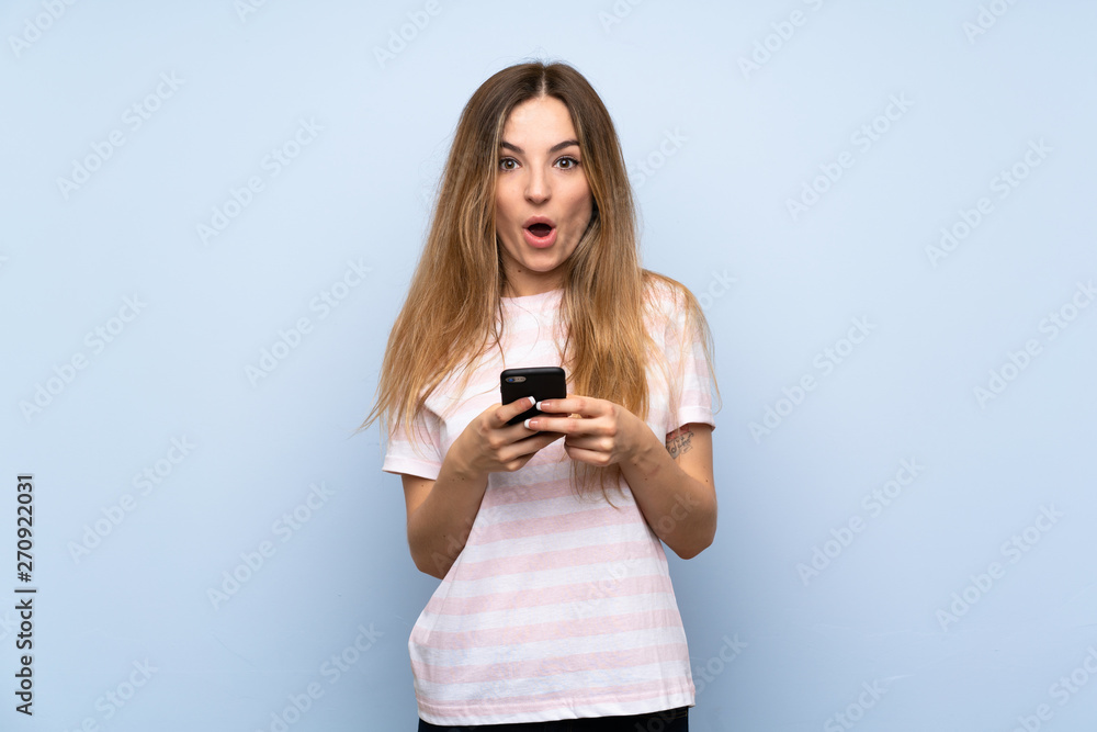 Young woman over isolated blue background surprised and sending a message Young woman over isolated blue background surprised and sending a message