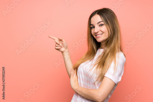 Young woman over isolated pink wall pointing finger to the side