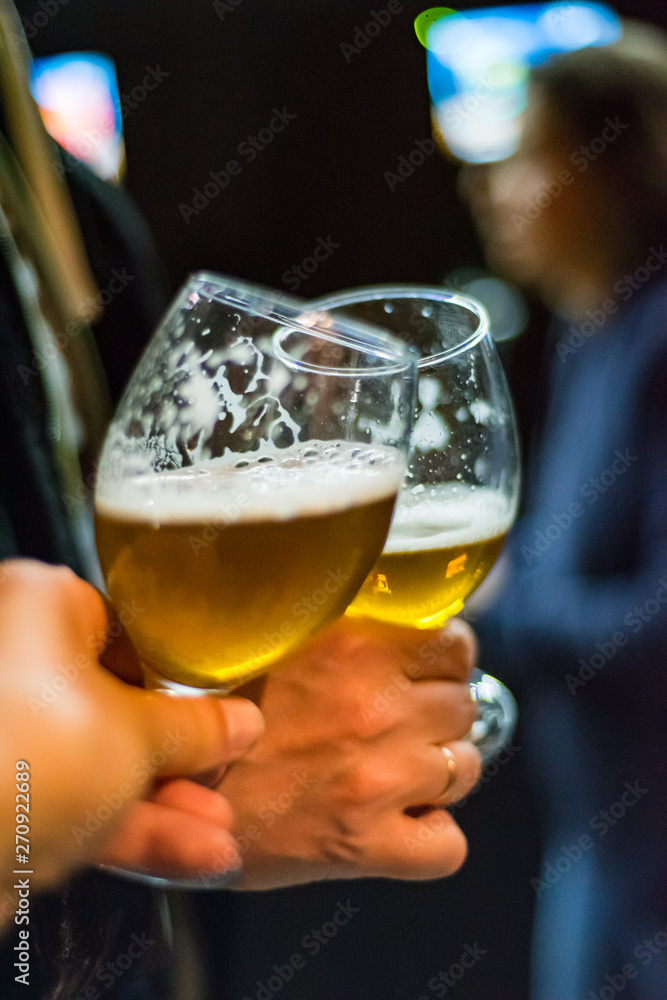 Close-up view of a two glass of beer in hand. Beer glasses clinking in bar or pub