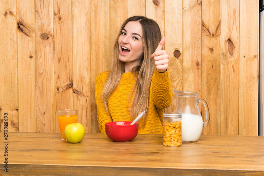 Young woman having breakfast in a kitchen with thumbs up because something good has happened Young woman having breakfast in a kitchen with thumbs up because something good has happened