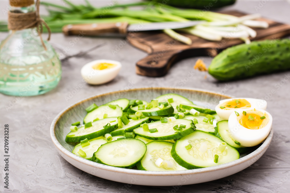 Fresh cucumber salad, boiled chicken eggs and green onions on a plate and ingredients for cooking on the table Fresh cucumber salad, boiled chicken eggs and green onions on a plate and ingredients for cooking on the table