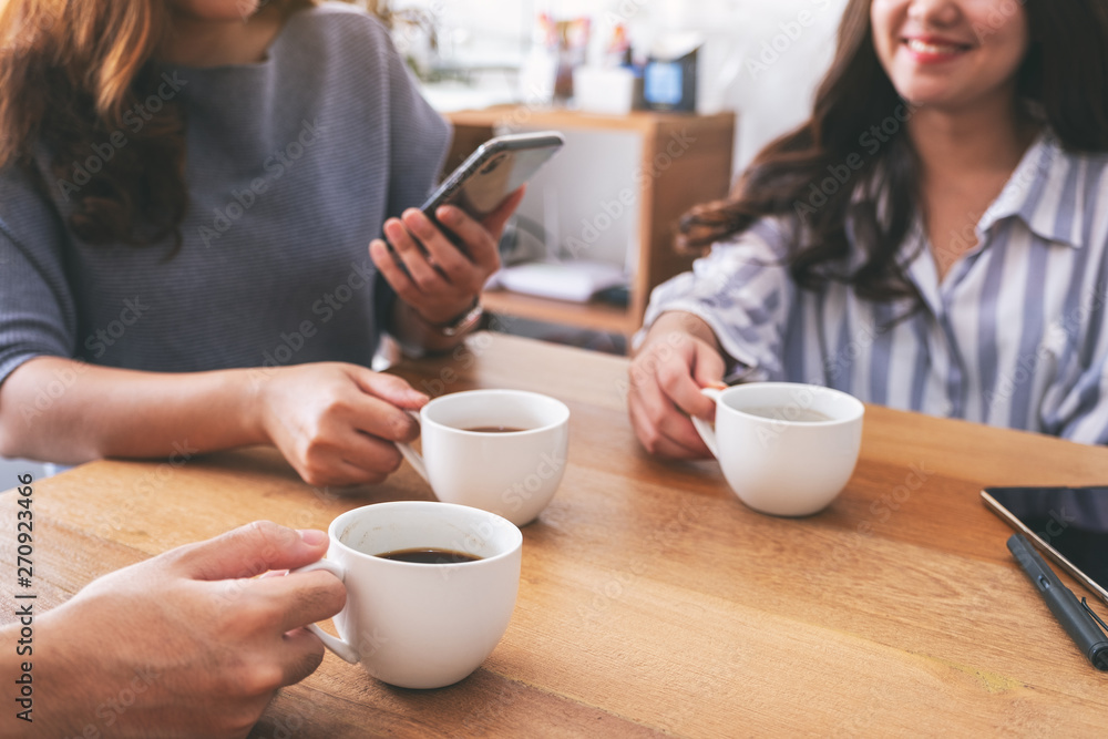 Closeup image of people using mobile phone and drinking coffee together Closeup image of people using mobile phone and drinking coffee together