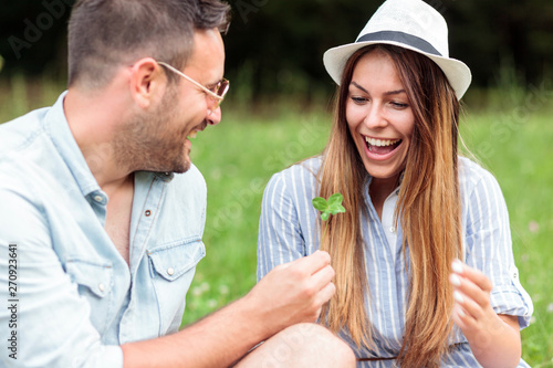 Smiling happy young couple spending time together on a picnic in park. Boyfriend giving four leaf clover to his girlfriend