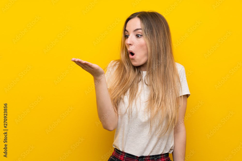 Young woman over isolated yellow wall holding copyspace imaginary on the palm Young woman over isolated yellow wall holding copyspace imaginary on the palm